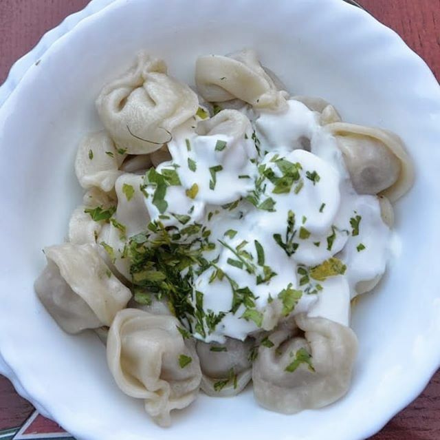 a white bowl filled with dumplings covered in sour cream and garnished with parsley