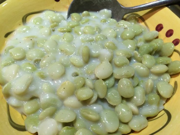 a yellow bowl filled with green beans on top of a table next to a spoon