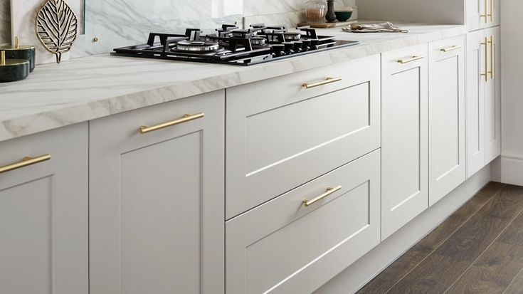 a white kitchen with marble counter tops and gold pulls on the cabinet doors is shown