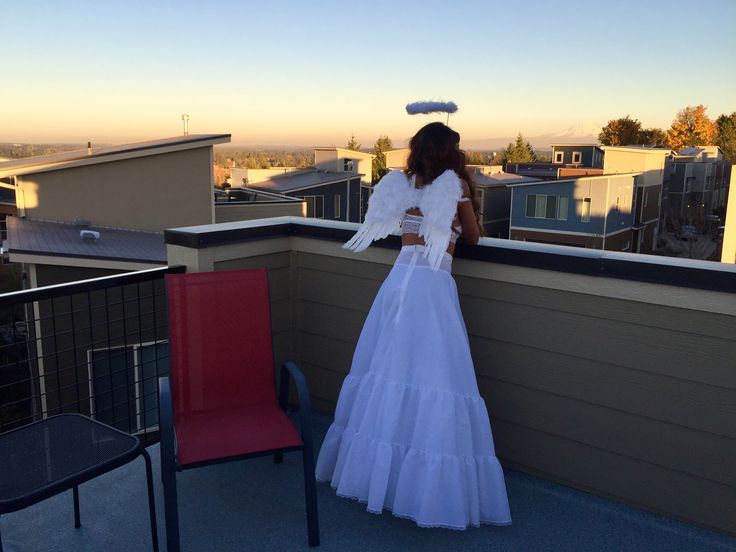 a woman in a white dress standing on top of a roof next to a red chair