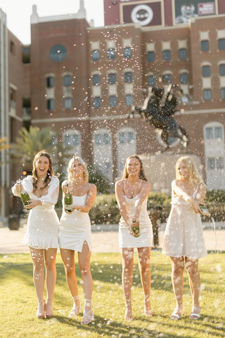 four women in white dresses are throwing confetti on each other and smiling at the camera