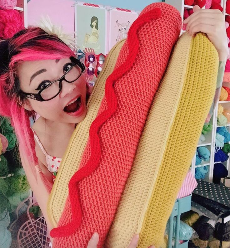 a woman with pink hair holding a giant hot dog in her hands and wearing glasses