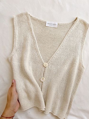 a woman's hand is holding up a white sweater with buttons on the front