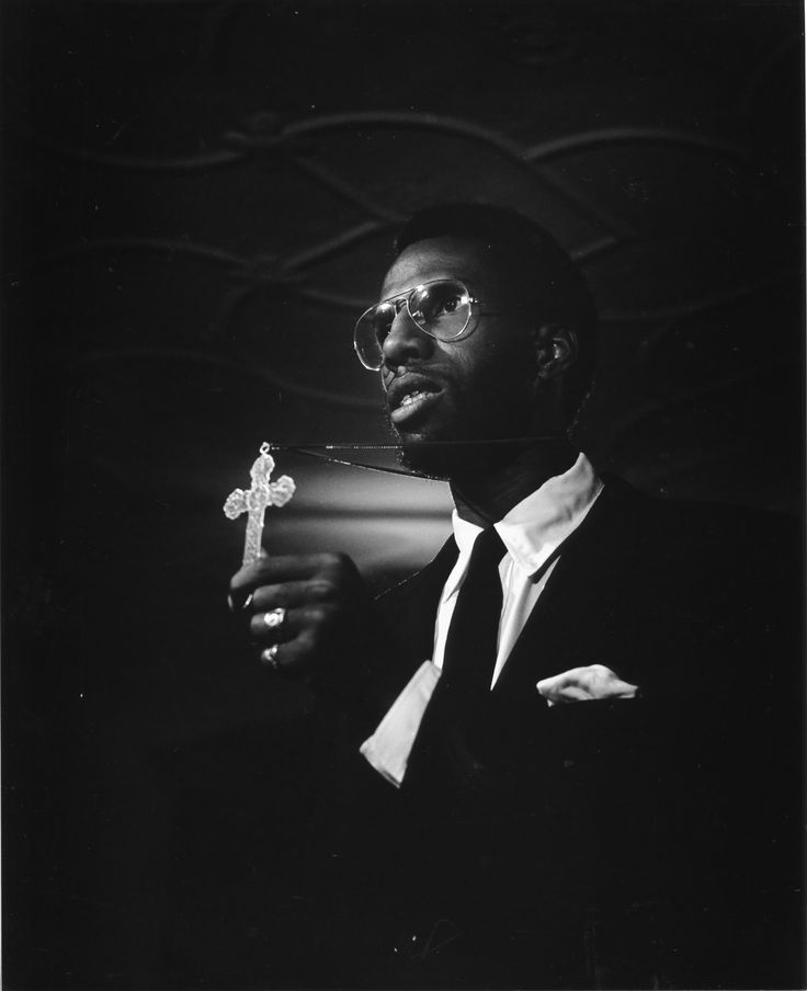 a black and white photo of a man in a suit holding a small crucifix