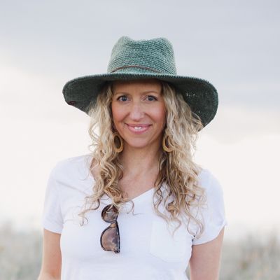 a woman wearing a hat and tie standing in front of the ocean with her hands on her hips