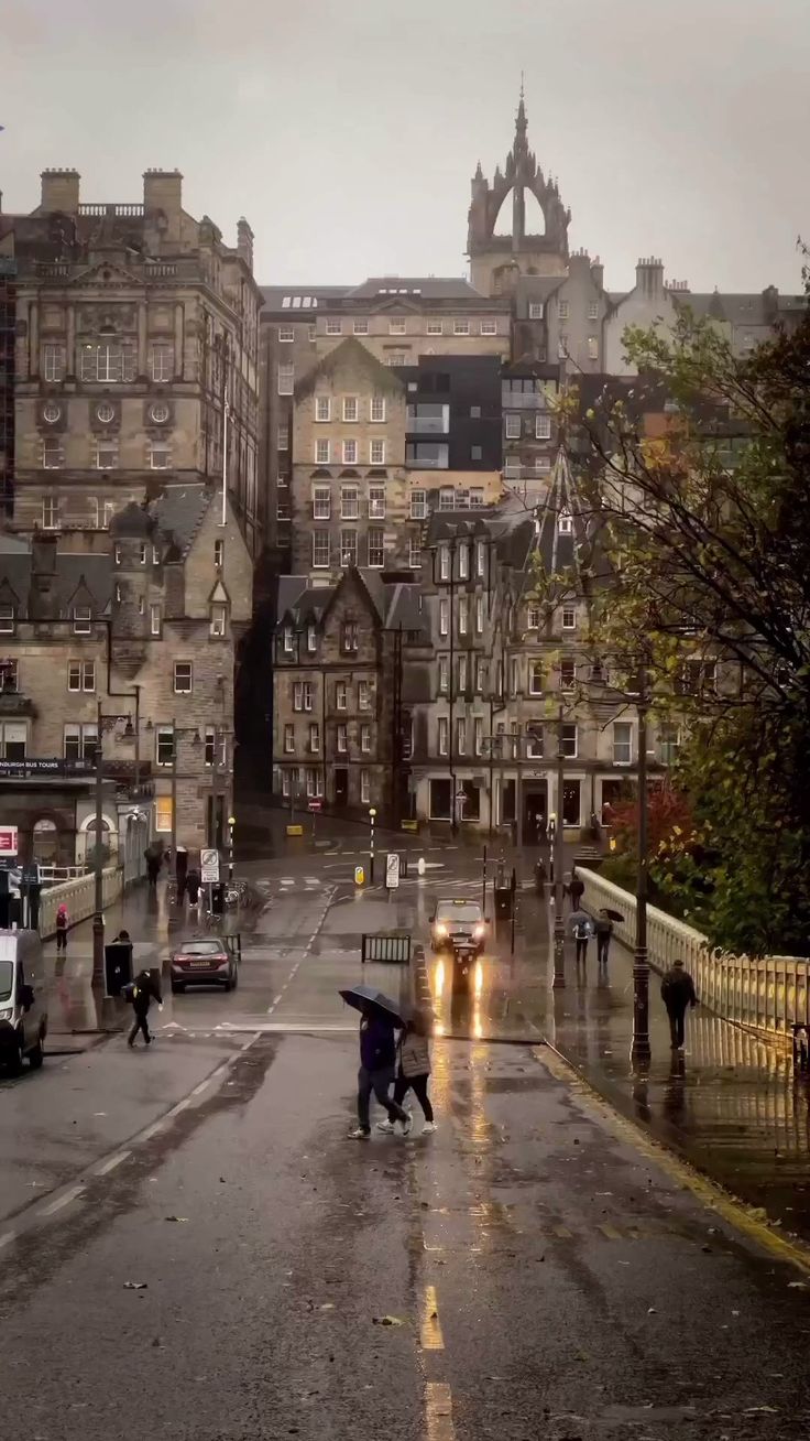 people are walking down the street with umbrellas in the rain and buildings behind them