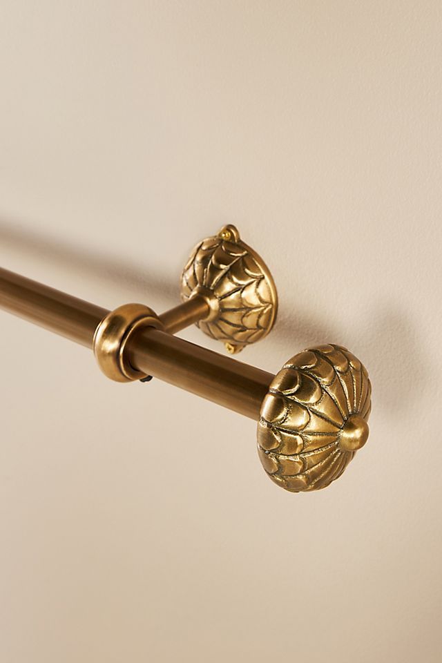 two gold handles on a white wall and a brown curtain rod with decorative leaves attached to it