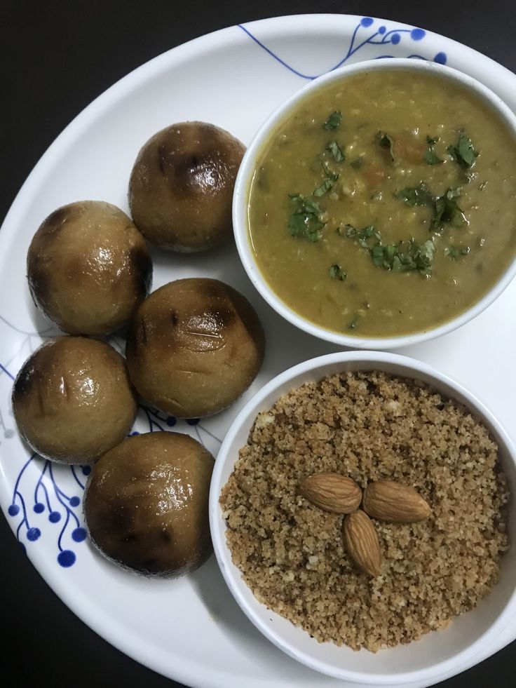 a white plate topped with three bowls filled with soup and two rolls covered in nuts