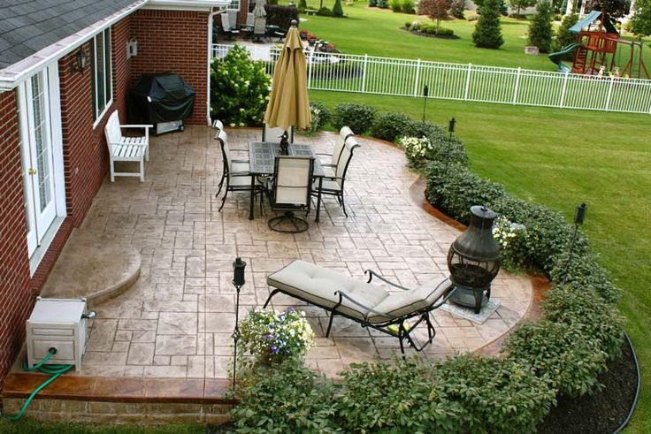 an outdoor patio with chairs, tables and umbrellas next to a brick walkway in the grass