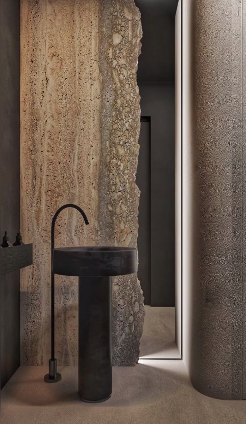 a black sink sitting next to a tall stone wall in a bathroom under a mirror