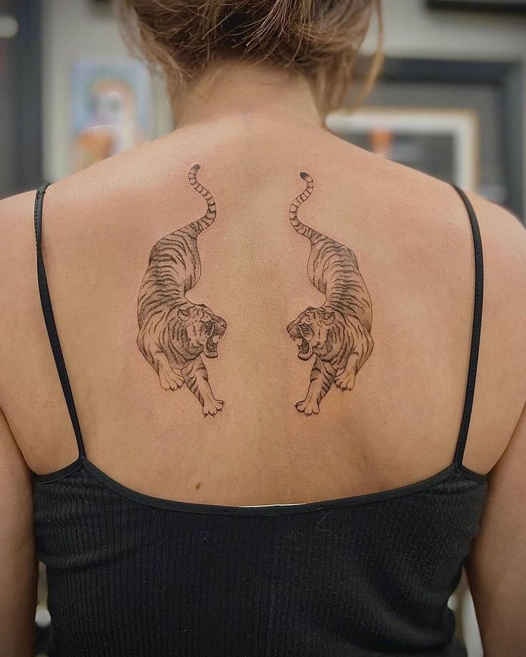 the back of a woman's neck with two tigers tattooed on her upper and lower back