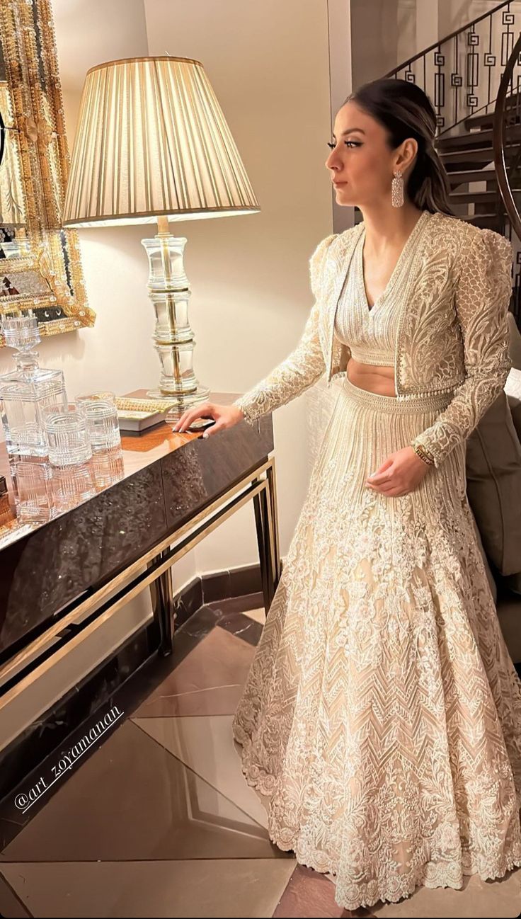 a woman standing in front of a table wearing a white dress and matching heels with her hand on top of the table