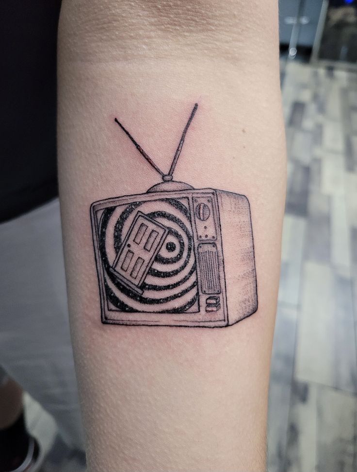 a black and white photo of a tv tattoo on the left arm, with an antenna in front of it