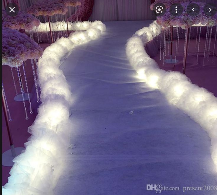 an aisle decorated with white feathers and pink flowers is lit up by fairy lights at the end