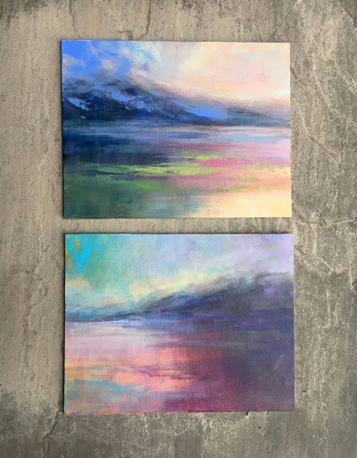 two paintings are shown on the concrete floor, one is blue and pink with white clouds