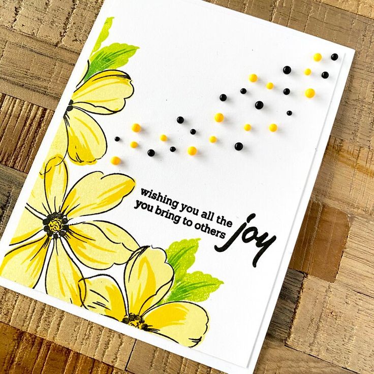 a card with yellow flowers on it and the words joy written in black ink, sitting on a wooden surface