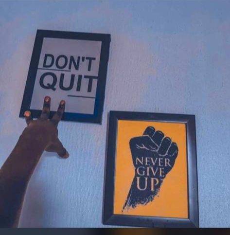 a giraffe is standing next to two framed posters and a sign that says, don't quit never give up