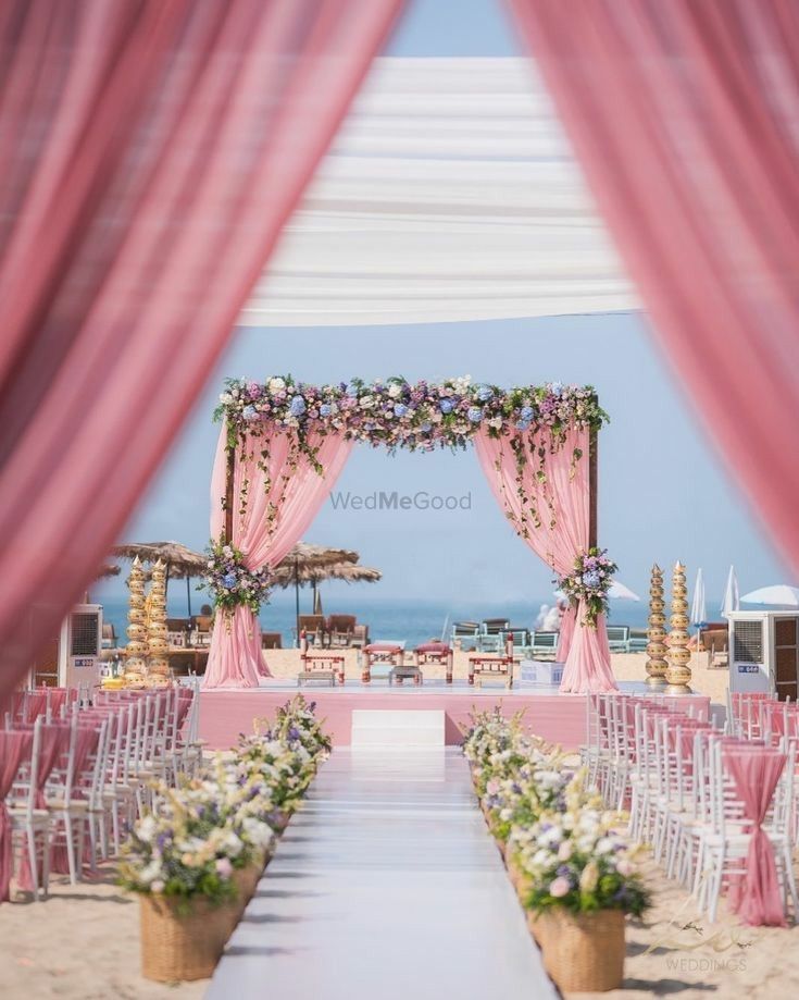 an outdoor ceremony set up with pink drapes and white flowers on the aisle to the beach