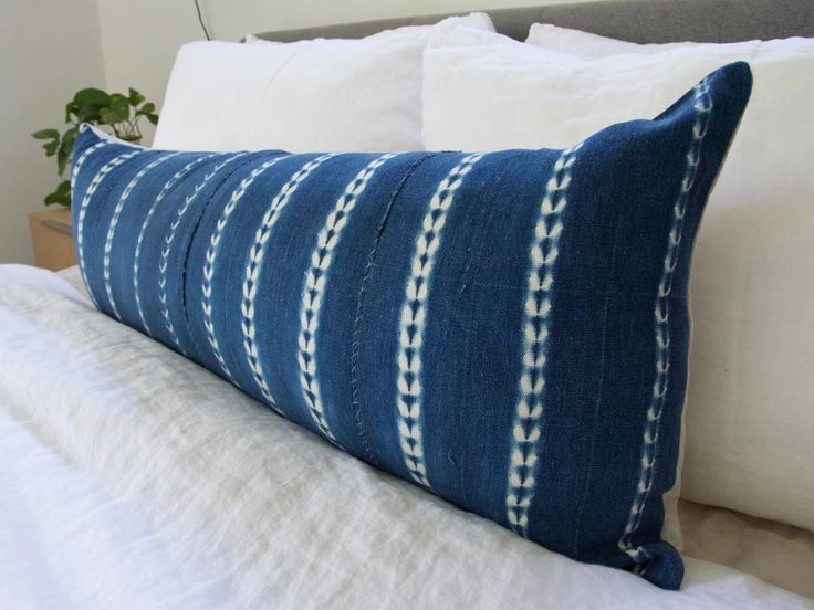 a blue and white striped pillow sitting on top of a bed next to a plant