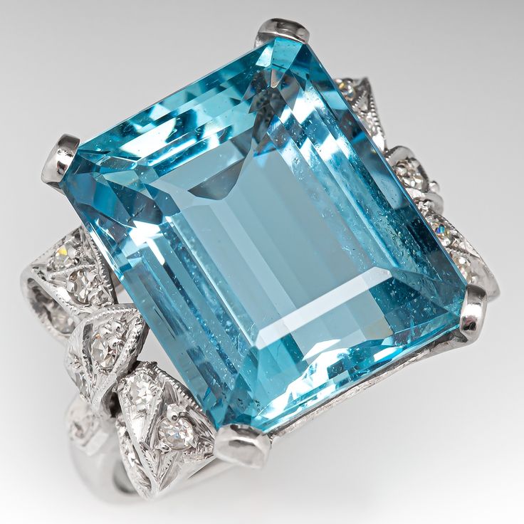 This striking vintage cocktail ring is centered with an emerald cut aquamarine, weighing 10.94 carats, in a four-prong setting. The shoulders are each accented with a bow design with milgrain details and is bead set with nine (9) round single cut diamonds. The ring measures 16.8mm at the top, rises 8.9mm above the finger, tapering to 1.9mm wide and 0.9mm thick at the base of the shank. This ring is currently a size 5. There is a tiny nick on the face of the stone. Aquamarine Stone Ring, Diamond Ring Platinum, Aquamarine Ring Vintage, Baguette Diamond Ring, Aquamarine Birthstone, Vintage Cocktail Ring, Baguette Diamond Rings, Diamond Cocktail Ring, Diamond Jewelry Designs