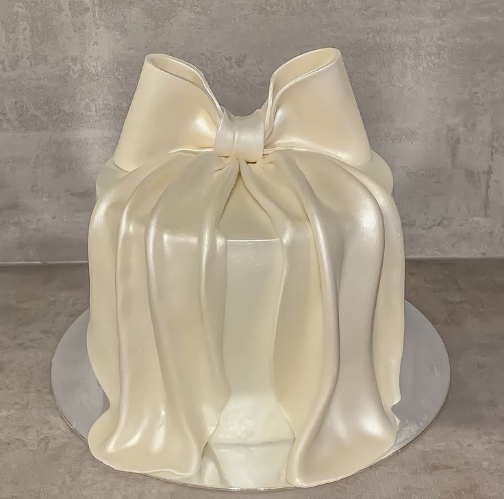 a white cake with a large bow on it's top sitting on a plate