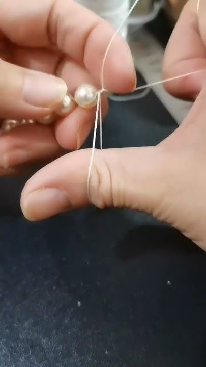 two hands are working on something with thread and pearls in the middle one hand is holding an object