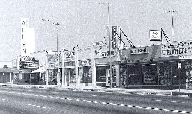 an old black and white photo of stores on the side of the road in front of some buildings