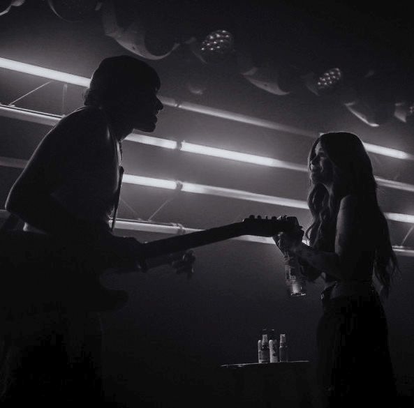 black and white photo of two people playing guitars in a dark room with spotlights