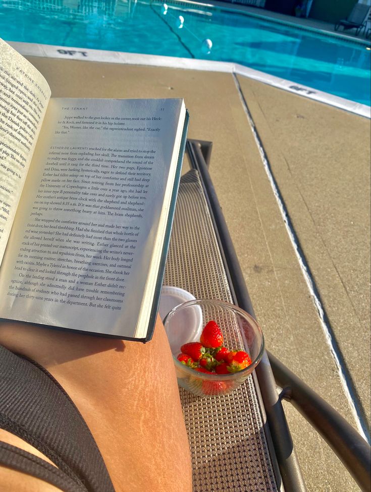 an open book sitting on top of a chair next to a swimming pool with strawberries in it