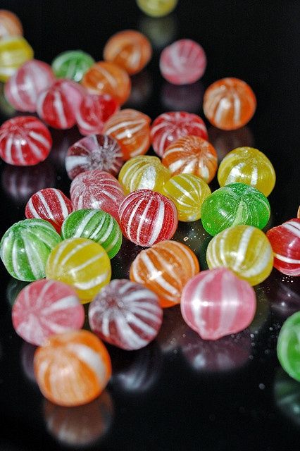 there are many different colored candy candies on the black counter top, all lined up together