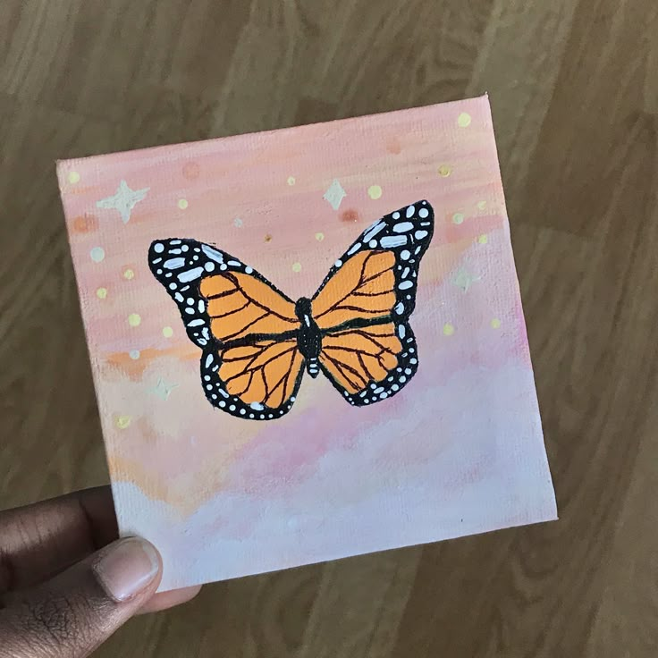 a hand holding up a piece of paper with a painting of a butterfly on it