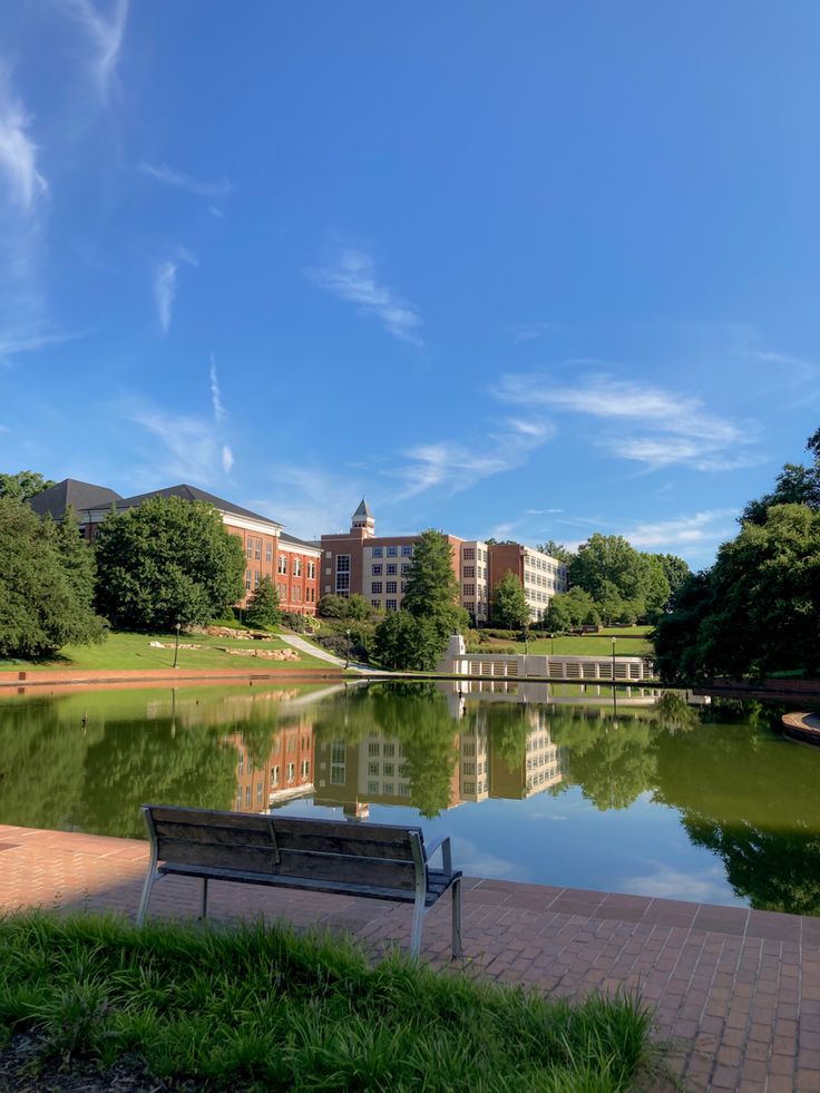 a bench sitting on the side of a lake in front of a large brick building