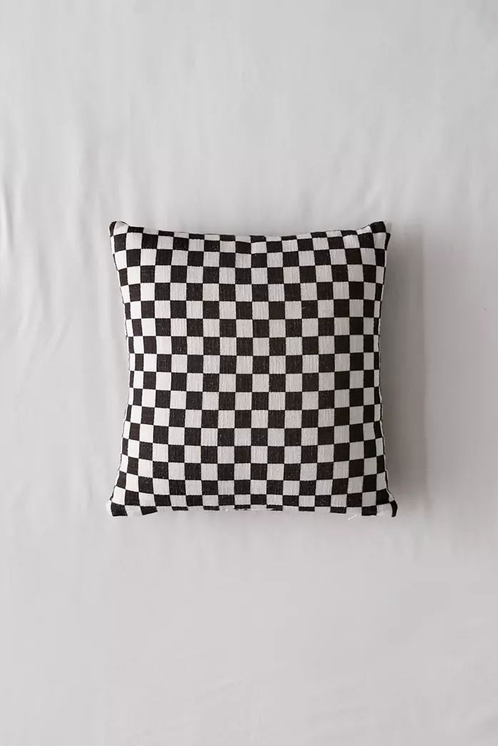 a black and white checkered pillow sitting on top of a bed next to a wall