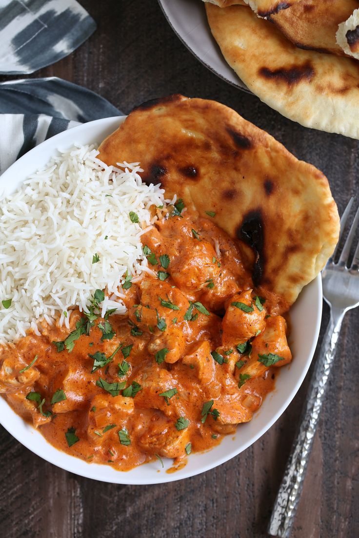 a white plate topped with rice and chicken next to naan bread on a wooden table