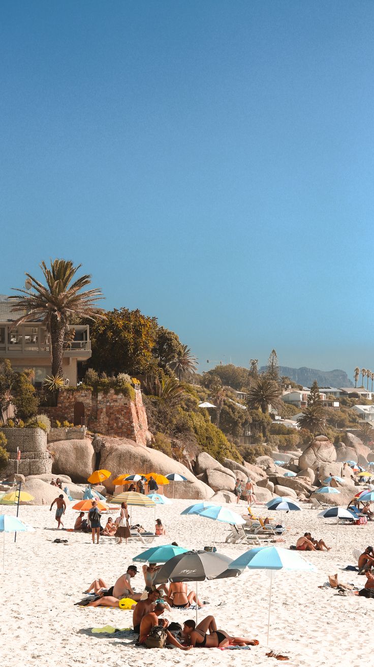 many people are laying on the beach under umbrellas