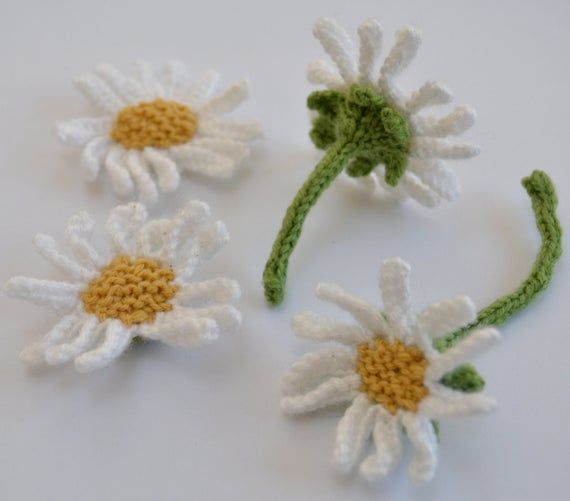 three crocheted white and yellow daisies on a white surface with green stems