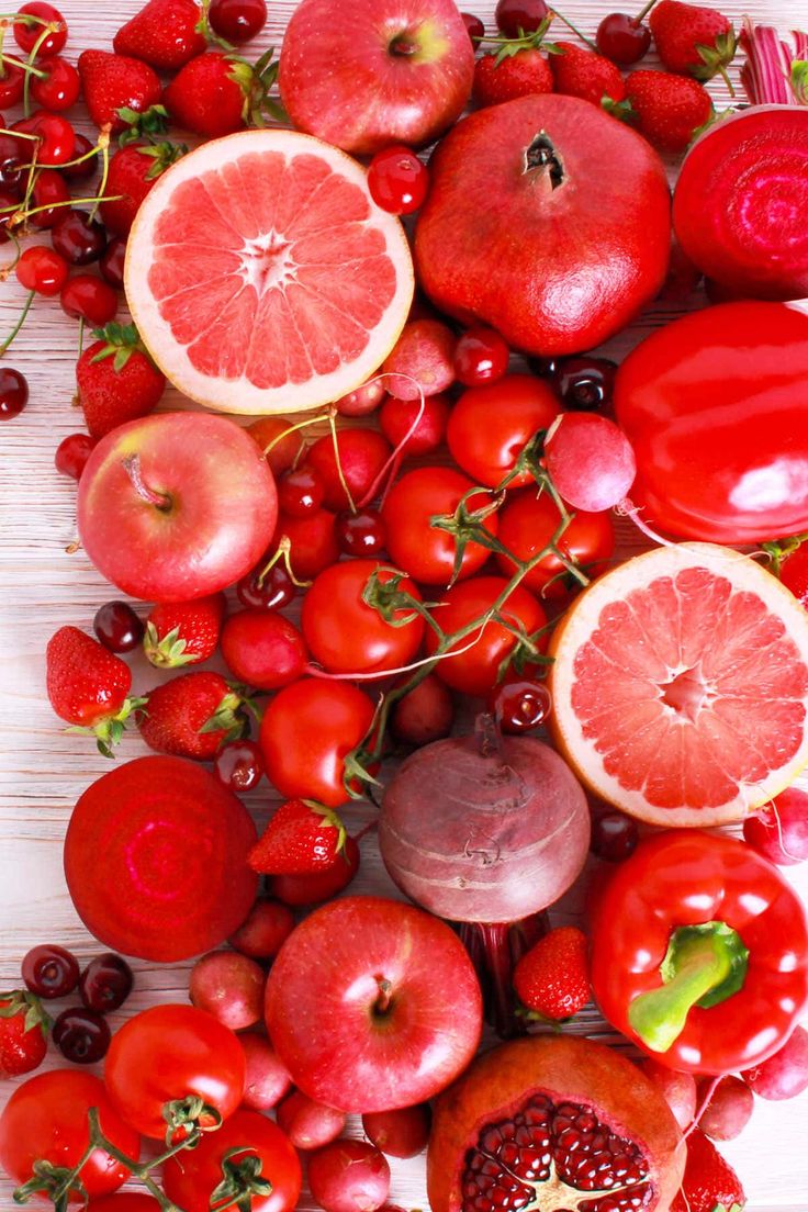 various fruits and vegetables are arranged on a white surface, including apples, tomatoes, pomegranates, cherries, and other fruit