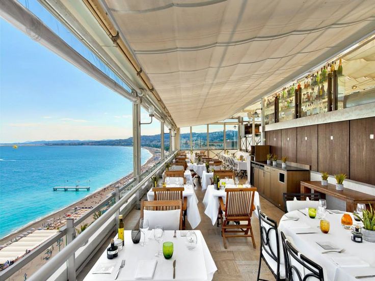 an outdoor dining area overlooking the ocean with tables and chairs set up for two people