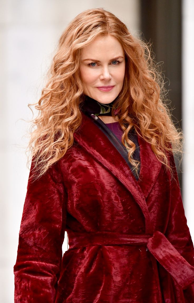 a woman in a red coat is walking down the street with her hair blowing back