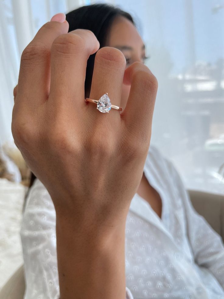 a woman is holding her hand up to the camera while wearing a diamond engagement ring