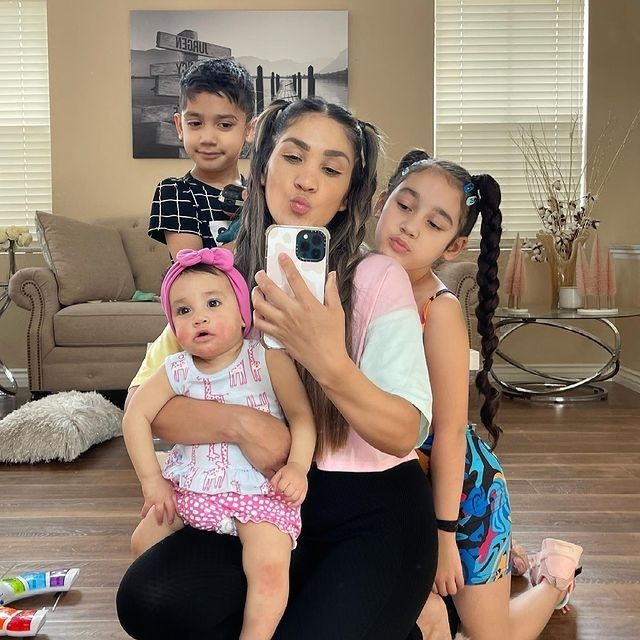 a woman taking a selfie with two children in front of her on the floor