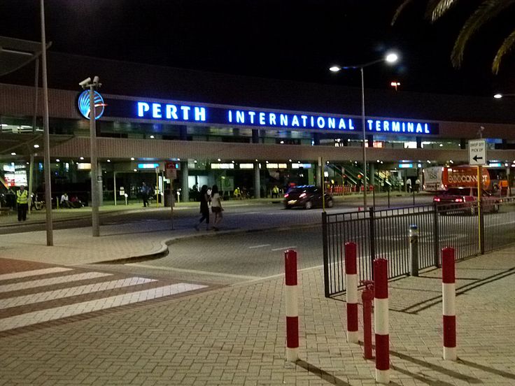 an airport terminal lit up at night with palm trees in the foreground and people walking on the sidewalk