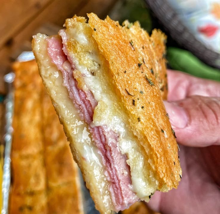 a person holding up a sandwich with meat and cheese on it in front of bread sticks