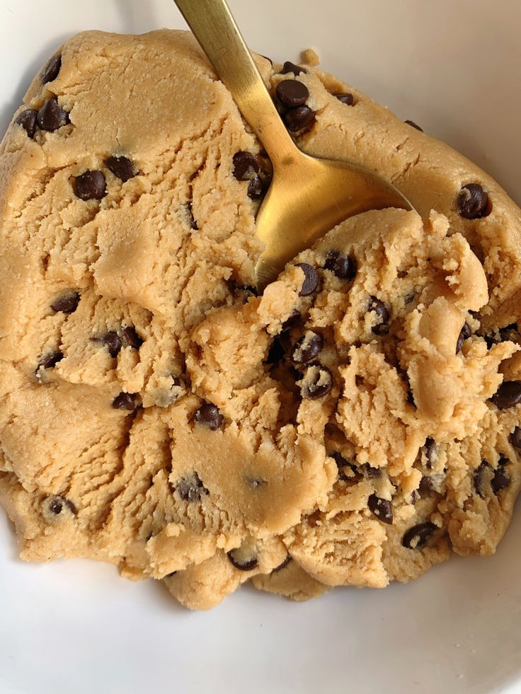 a scoop of ice cream in a white bowl with chocolate chips on it and a gold spoon