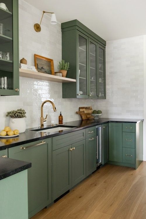 a kitchen with green cabinets and wood flooring is pictured in this image, there are shelves on the wall above the sink