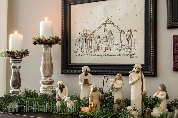 a christmas mantel with figurines and candles in front of a framed nativity scene