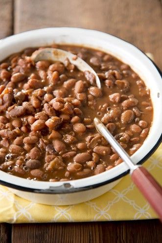 a white bowl filled with baked beans on top of a yellow napkin next to a wooden table