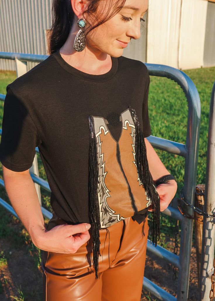 Get ready to ride with the Buck Around Fringe Chaps Tee! This playful tee features a unique design with bucking broncos, chaps, and rodeo-inspired "let em ride" text. Perfect for any cowboy or cowgirl looking to add a quirky and fun touch to their wardrobe. Yee-haw! Casual T-shirt For Western-themed Fall Events, Fall Ranch Crew Neck T-shirt, Western Tops For Rodeo In Fall, Western Style Tops For Rodeo In Fall, Western Style T-shirt For Rodeo, Western Style T-shirt For Fall Western-themed Events, Western-style T-shirt For Western-themed Fall Events, Fitted Crew Neck T-shirt For Rodeo, Graphic Tee For Western-themed Fall Events