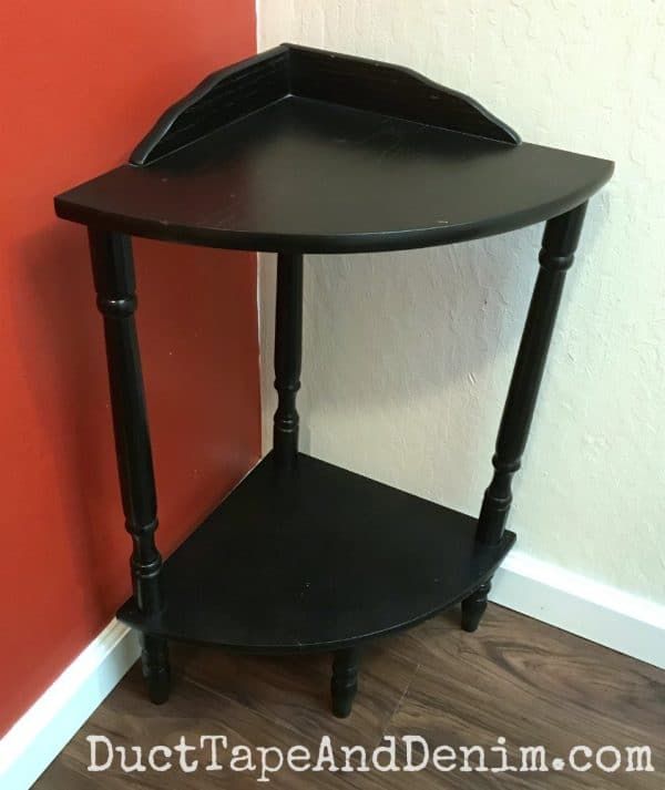 a black corner table sitting on top of a hard wood floor next to a red wall