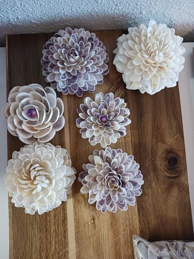 several different types of paper flowers on a wooden board with white and purple colors in the center